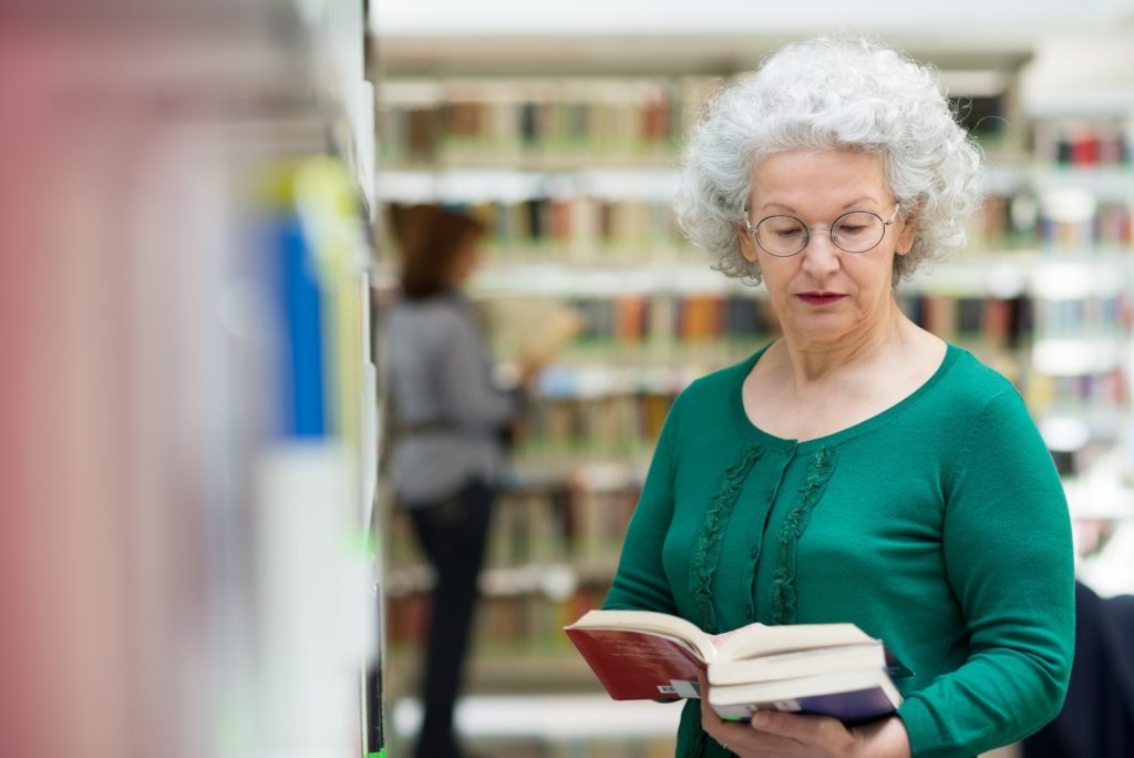 Senior Woman Reading And Choosing Book In Library